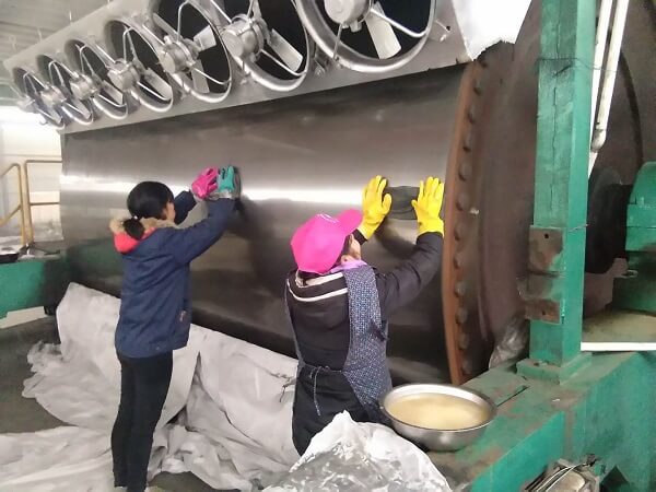 济南天盟公司现场施工的浙江某新纸业的烘缸喷涂工程最后一个环节"养缸"完成，工人正在擦除表面保养油脂